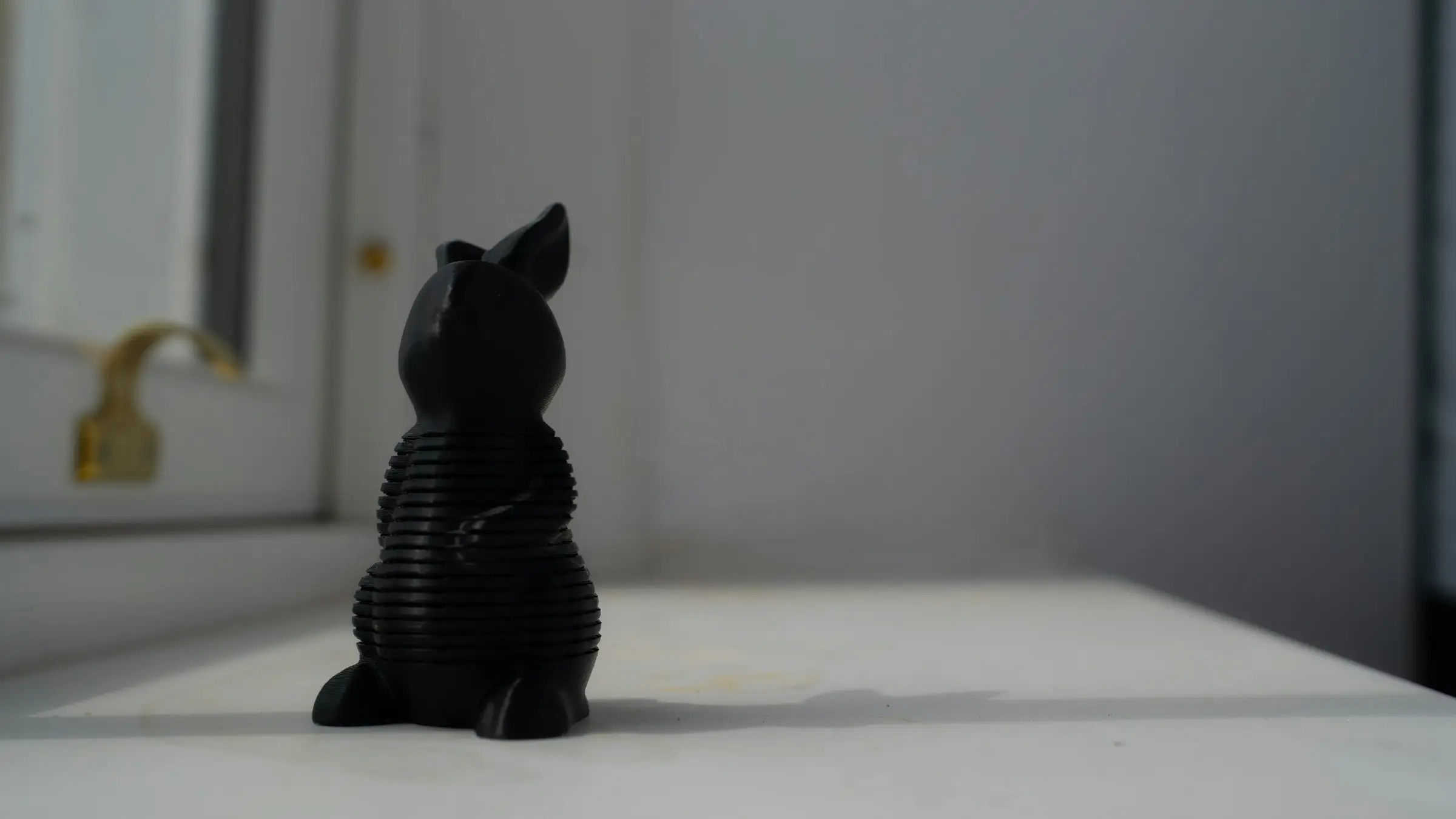 A small black 3D printed rabbit figure with visible layer lines standing on a white windowsill.