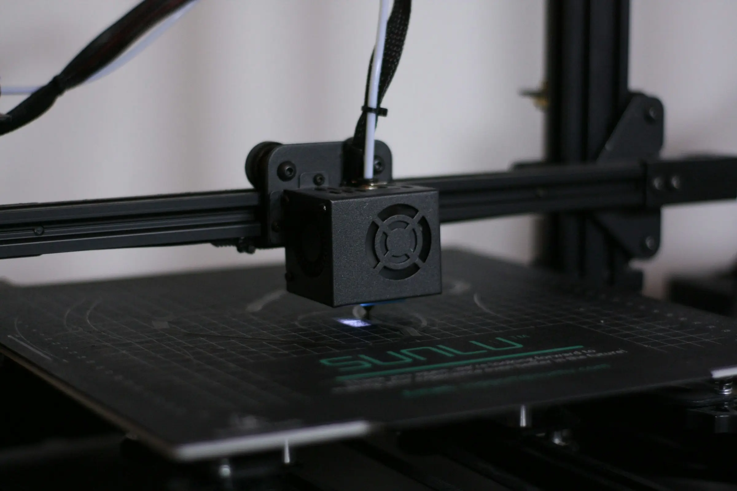 A black print head with a fan shroud hovering just above an empty gridded print bed.