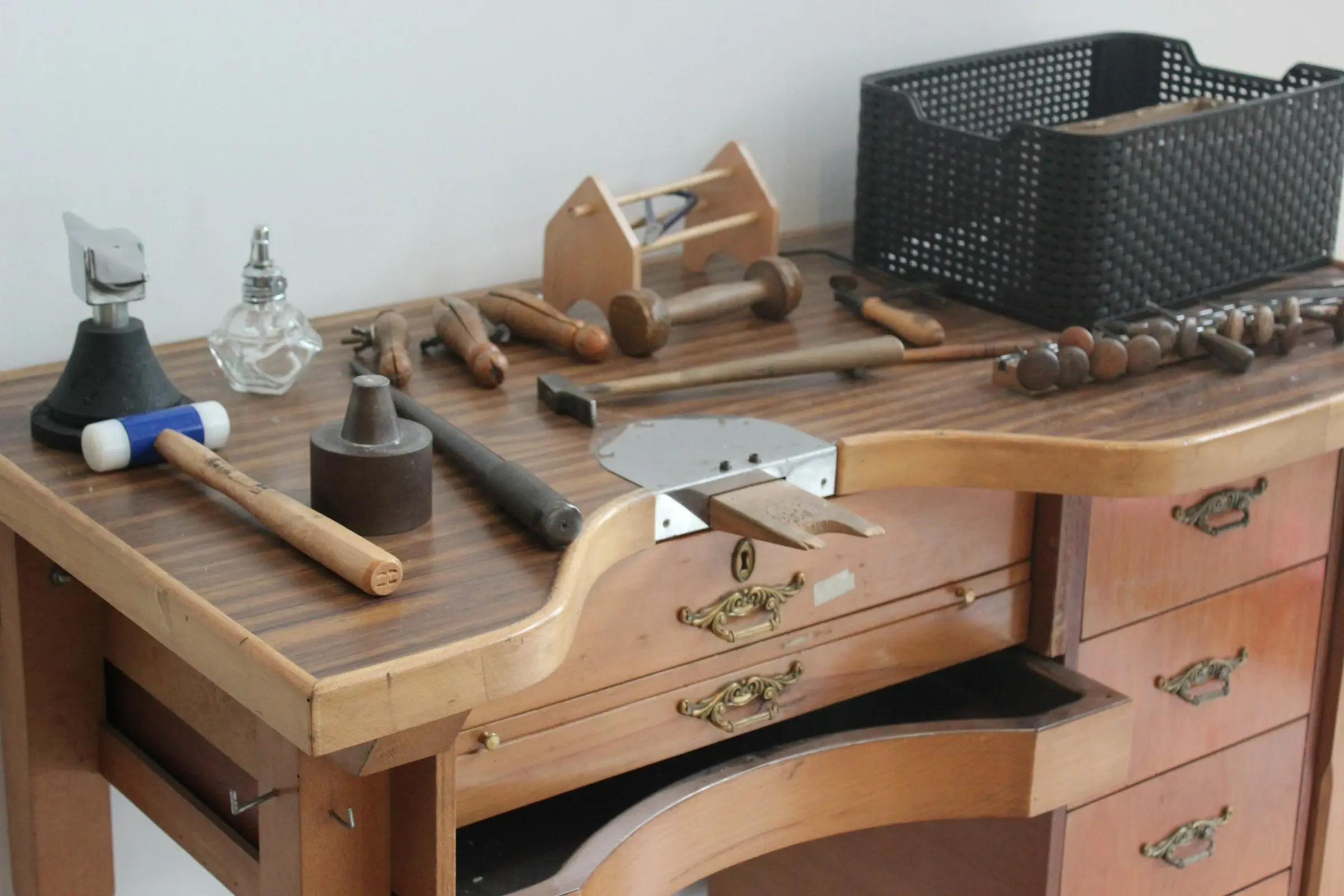 A wooden craft workbench with mallets, hammers, files and a small vice laid out on top.